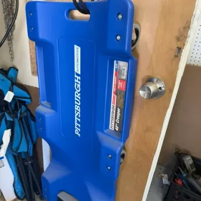 Pittsburgh Automotive 40-inch molded plastic mechanic's creeper in blue, hanging on a door hook in good condition.