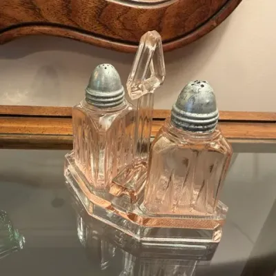 Vintage pink depression glass salt and pepper shaker set with metal caps in a matching glass holder.