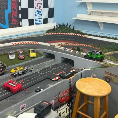 Large custom slot car racing track setup featuring multiple lanes, scenery details, and assorted slot cars.