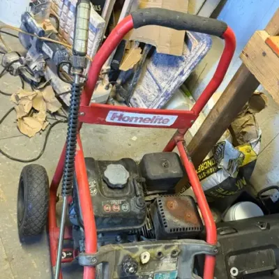 Red Homelite gas-powered pressure washer with wheeled tubular frame, spray wand, and attached engine.