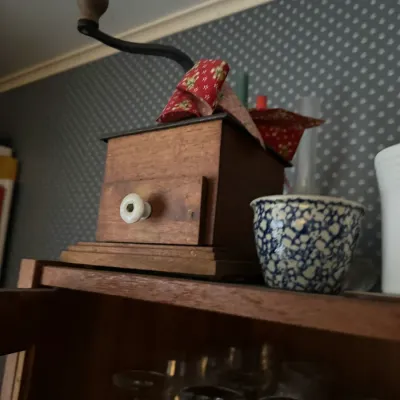 Sale Photo Thumbnail #115: Vintage wooden hand-crank coffee grinder with a ceramic drawer pull, displayed alongside a blue and white patterned ceramic teacup.