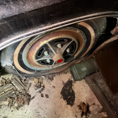 Sale Photo Thumbnail #32: Flat whitewall tire mounted on a rusted classic car wheel with a red center cap, showing heavy surface wear and cobwebs.