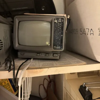 Sale Photo Thumbnail #167: Vintage Coby small portable black and white television and radio set, sitting on a shelf alongside other vintage electronics.