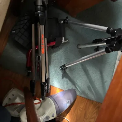 Sale Photo Thumbnail #96: Slik U7000 camera tripod shown alongside a secondary silver tripod and a small hand vacuum resting on carpeted flooring.