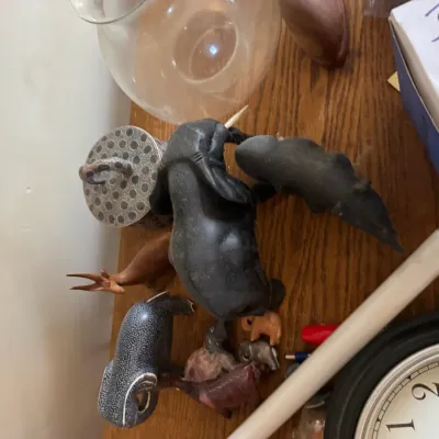 Sale Photo Thumbnail #127: Collection of carved animal figurines, including ebony elephants, a rhinoceros, and hand-painted decorative pieces, displayed on a wooden surface.