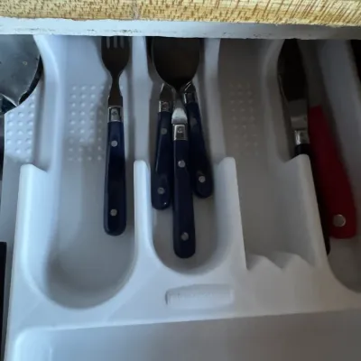 Sale Photo Thumbnail #67: White plastic Rubbermaid cutlery drawer organizer containing a partial set of blue riveted-handle flatware and a red utility knife.