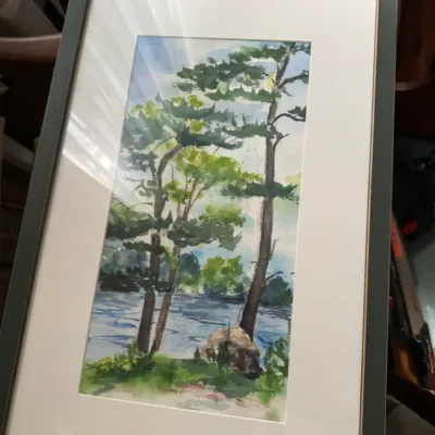 Sale Photo Thumbnail #98: Original watercolor painting depicting pine trees by a lake, presented in a dark green frame with white matting.