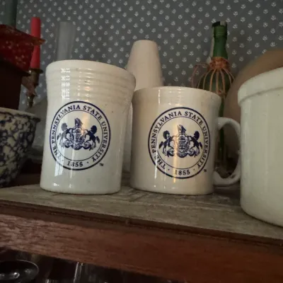 Sale Photo Thumbnail #113: Pair of off-white stoneware mugs featuring The Pennsylvania State University seal logo in blue.