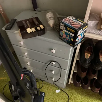 Sale Photo Thumbnail #37: Small painted wood five-drawer chest holding various household miscellany, alongside a shoe rack and an upright vacuum cleaner.