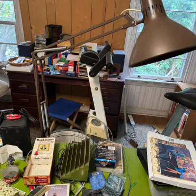 Sale Photo Thumbnail #50: Vintage brown metal spring-arm task desk lamp mounted over a workspace filled with assorted office supplies, media, and collectibles.