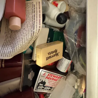 Sale Photo Thumbnail #57: A cluttered drawer filled with various toiletries, promotional flyers, hotel soaps, and plastic containers.