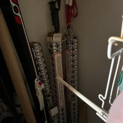 Sale Photo Thumbnail #85: Vintage Rossignol downhill skis with bindings stored alongside a pair of ski poles and boxed Kirsch curtain rods in a closet corner.