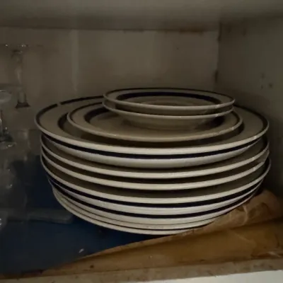 Sale Photo Thumbnail #64: Stack of mid-century ceramic dinnerware plates and small bowls with dark trim, stored inside a cabinet.
