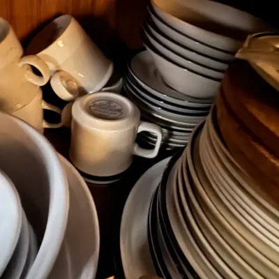 Sale Photo Thumbnail #119: Collection of vintage stoneware and ceramic dinnerware, including stacks of plates, bowls, and matching mugs stored inside a wooden cabinet.