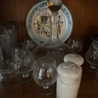 Sale Photo Thumbnail #110: Collection of glassware including snifters and a ship-etched decanter, accompanied by a pair of white ceramic salt and pepper shakers and a hand-painted Italian ceramic plate.