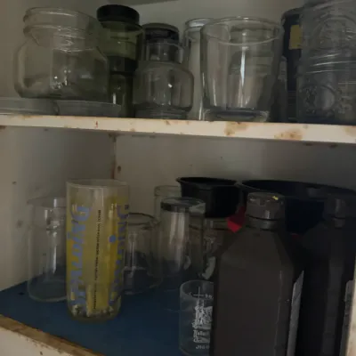 Sale Photo Thumbnail #62: Assorted glassware, vintage mason jars, and chemical bottles stored on white wooden cabinet shelves.