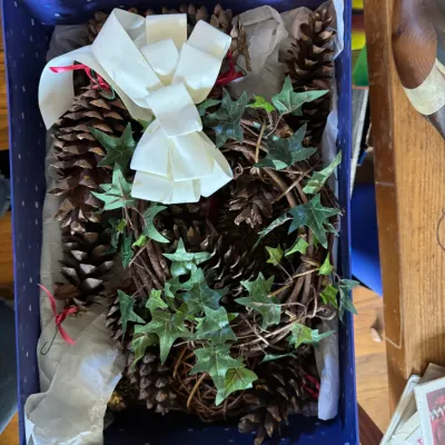 Sale Photo Thumbnail #124: Box of holiday decor featuring natural pinecones, faux ivy, and a large cream-colored bow.