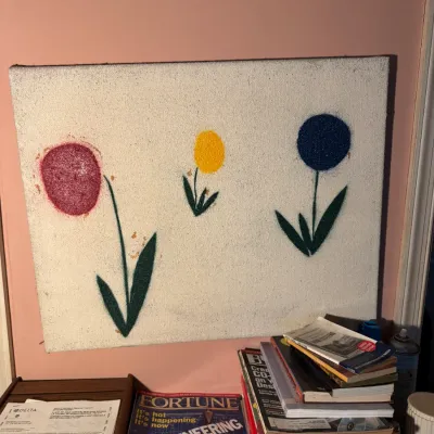 Sale Photo Thumbnail #79: Mid-century minimalist canvas wall art depicting three colorful stylized flowers, resting above stacks of vintage magazines and books.