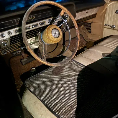 Sale Photo Thumbnail #31: Interior view of a vintage 1960s Ford automobile, showing a weathered steering wheel, dashboard controls, and vinyl bench seat with a mesh cover.