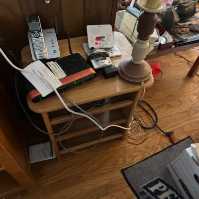Sale Photo Thumbnail #133: Small oak side table featuring various home electronics including a VTech cordless phone system, internet router, digital clock, and a candlestick-style table lamp.