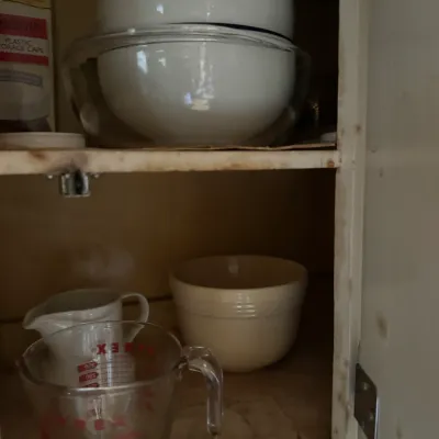 Sale Photo Thumbnail #63: Assorted vintage kitchenware including a Pyrex glass measuring cup, ceramic pitcher, and nesting mixing bowls displayed inside a cabinet.