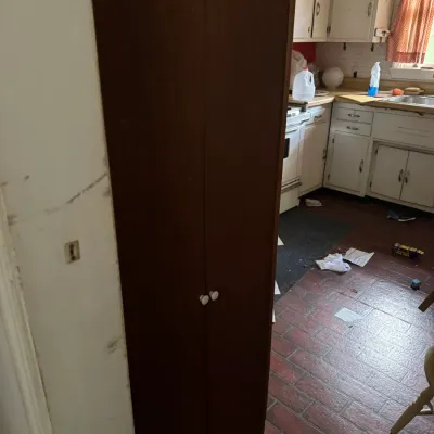 Sale Photo Thumbnail #59: Tall dark wood two-door storage cabinet standing in a kitchen.