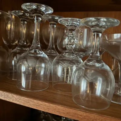 Sale Photo Thumbnail #112: Collection of clear crystal and glass stemware, including wine goblets and faceted stem glasses, stored upside down on wooden shelves.