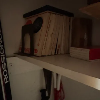 Sale Photo Thumbnail #82: Collection of vintage books held by a metal bookend on a shelf, alongside Rossignol ski equipment.