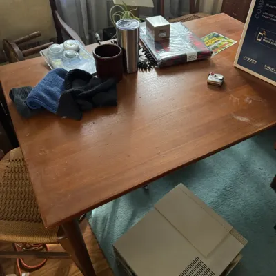 Sale Photo Thumbnail #16: Mid-century wooden dining table holding various household items, flanked by woven-seat chairs.