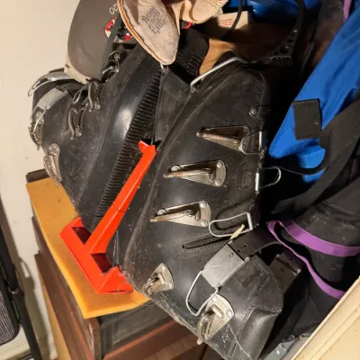 Sale Photo Thumbnail #80: Vintage black hard-shell ski boots with metal buckles, shown resting on a shelf alongside assorted winter gear.