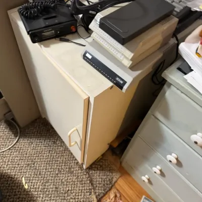 Sale Photo Thumbnail #69: Collection of vintage computer peripherals and electronics, including a stack of dial-up modems and a CB radio unit atop a small cabinet.