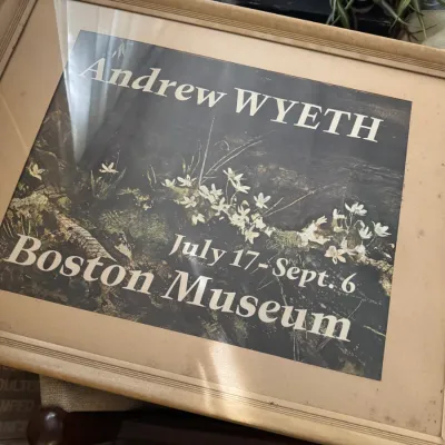 Sale Photo Thumbnail #99: Framed exhibition poster for Andrew Wyeth at the Boston Museum, featuring a dark botanical illustration under glass with a tan mat and light wood frame.