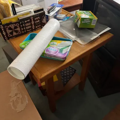Sale Photo Thumbnail #101: Assorted household supplies including Swiffer Sweeper refills, a poster tube, and office items displayed on an oak end table.