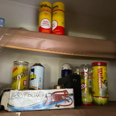 Sale Photo Thumbnail #26: Collection of shelf items including Wilson Championship tennis ball cans, a boxed hi-volume 100 PSI foot pump, and household spray cans.