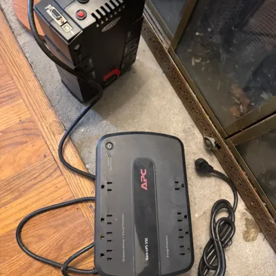 Sale Photo Thumbnail #157: APC Back-UPS 550 battery backup and surge protector resting on the floor next to a second black electronics unit.