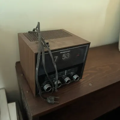 Sale Photo Thumbnail #154: Vintage Magnavox digital flip clock AM/FM radio with a faux-woodgrain casing, featuring silver control knobs and an attached power cord.
