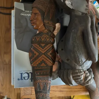Sale Photo Thumbnail #128: Two hand-carved wooden tribal sculptures, including a flat geometric wall relief bust and a full-body standing figure.