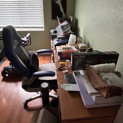 Home office setup featuring a blue and white gaming-style swivel chair alongside a wooden desk holding electronics, boxed items, and...