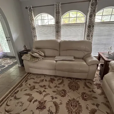 Off-white leather reclining sofa paired with a large floral area rug in beige and brown tones.