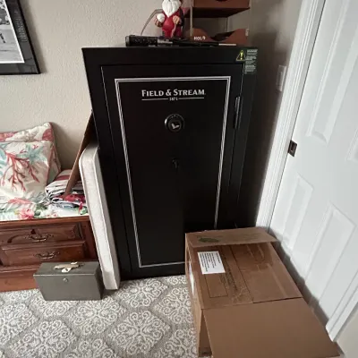 Large black Field & Stream gun safe with white trim, shown alongside a smaller metal lockbox and a cardboard box.