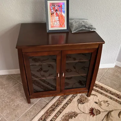 Dark wood media console cabinet featuring two glass-front doors with silver hardware, topped with a digital photo frame.