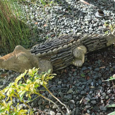 Rustic stone and concrete alligator garden sculpture featuring layered stone tile accents along its body.