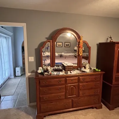Traditional wooden bedroom dresser featuring a attached tri-fold arched mirror and multiple storage drawers, shown alongside a matching...