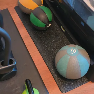 Collection of home gym equipment including three rubber medicine balls of various weights and a bright green kettlebell resting on...