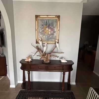 Traditional dark wood console table with two drawers and a bottom shelf, topped with a driftwood heron sculpture, sea shells, and a...