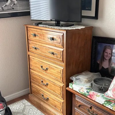 Traditional oak tallboy chest of drawers featuring ornate metal bail handles, molded panel drawer fronts, and a Samsung flat-screen TV on...