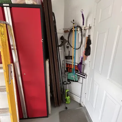 A collection of garage equipment and household supplies including a yellow stepladder, a red metal storage cabinet, folding tables, and...
