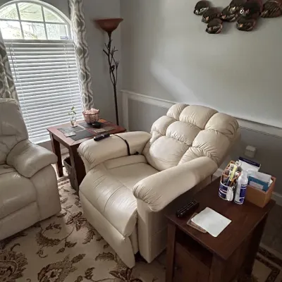 Contemporary off-white leather power lift recliner with overstuffed tufting, shown alongside dark wood end tables in a living room setting.