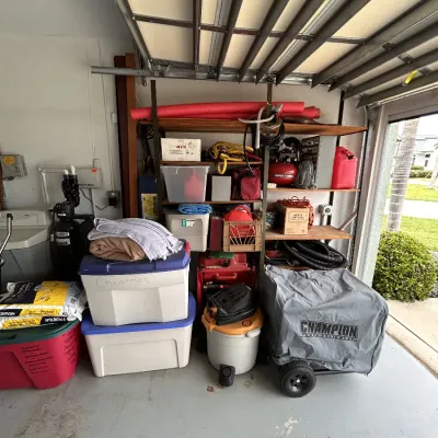 Garage filled with various household and utility items, including plastic storage totes, a Champion portable generator with cover, a shop...
