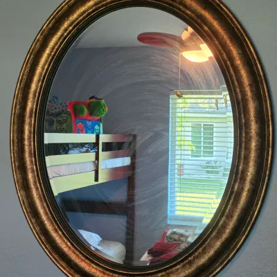 Large oval wall mirror in a textured gilt brass or molded gold-tone frame.